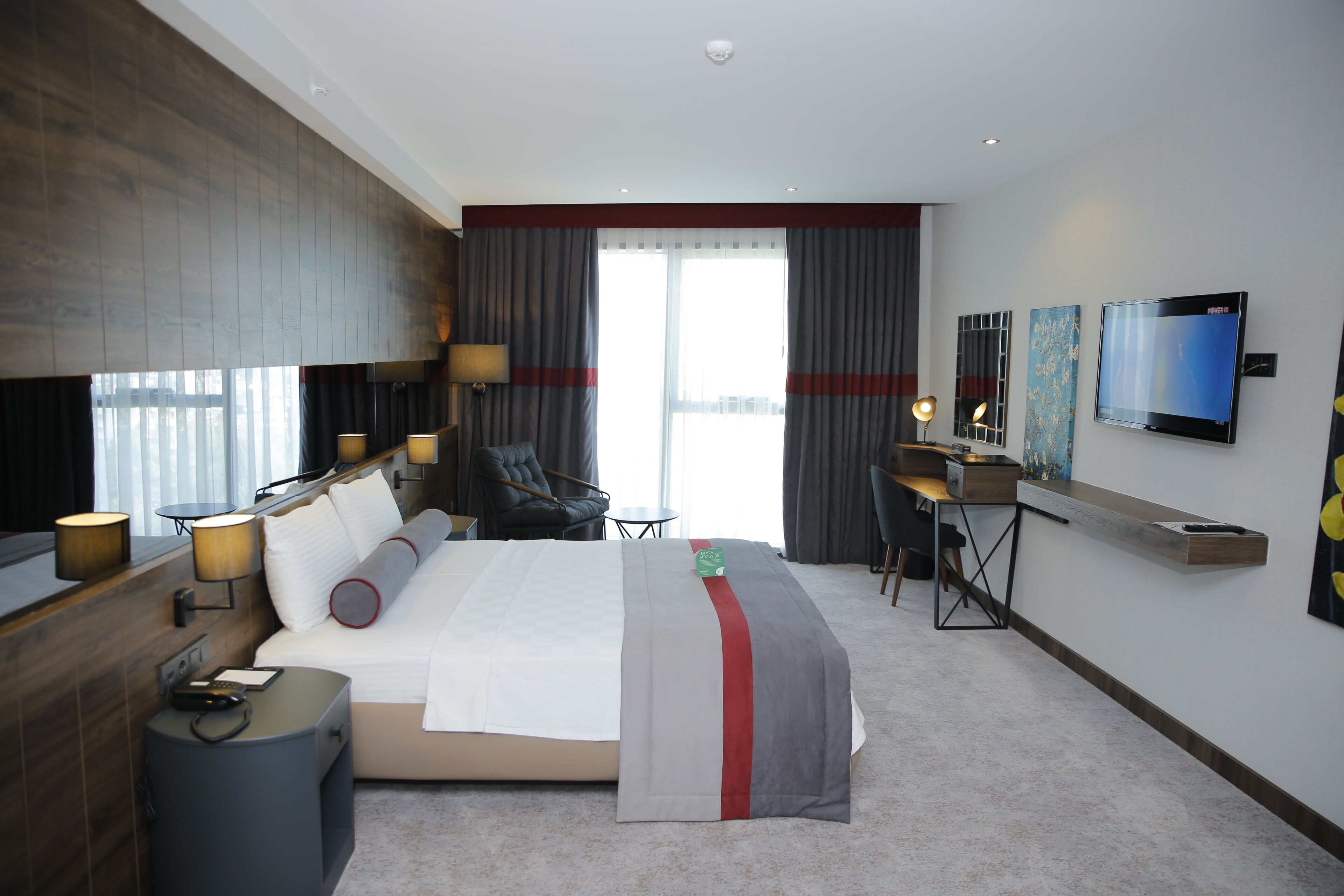 A modern hotel room with a large bed, a desk, a chair, and a TV.