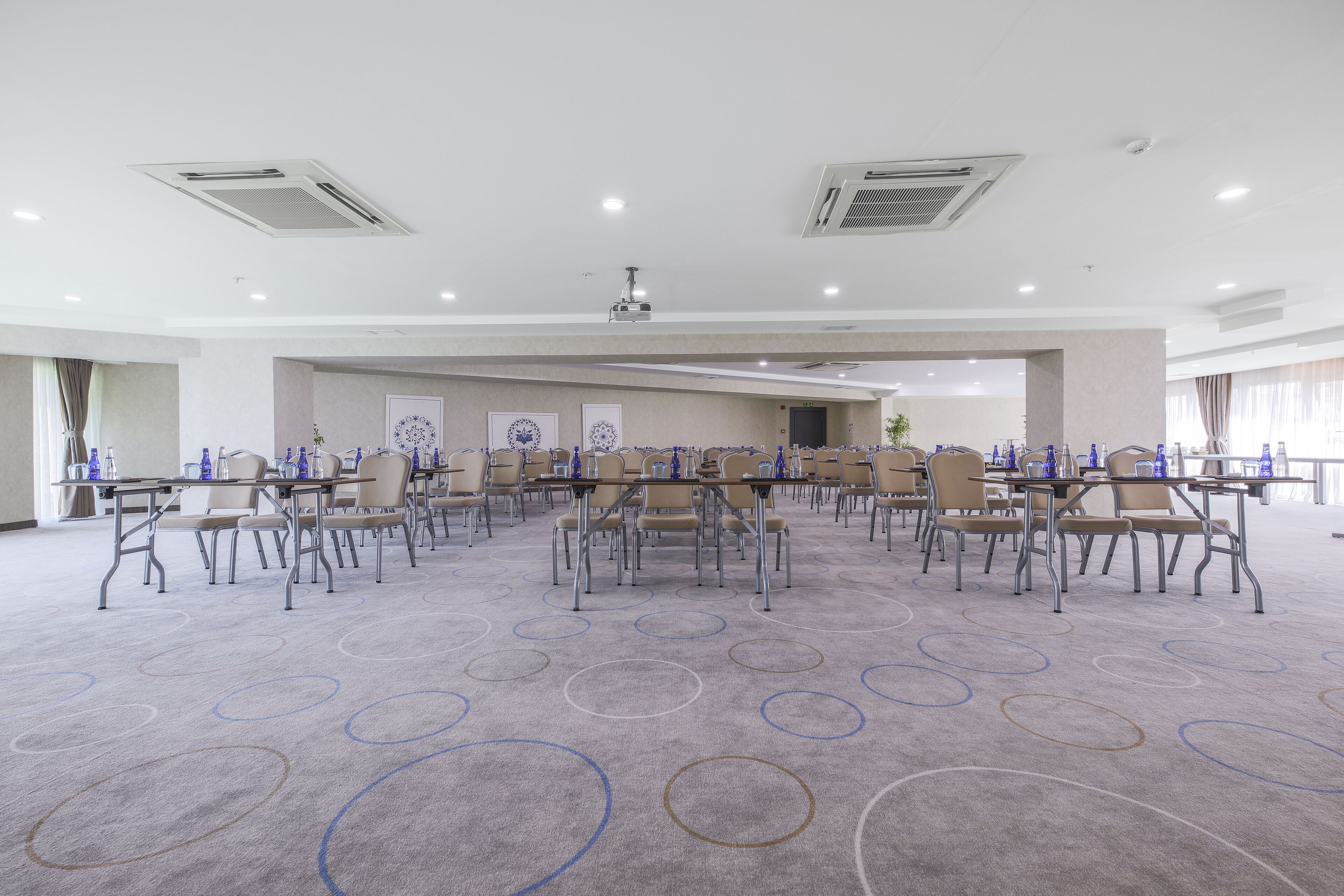 A large conference room with multiple tables and chairs, equipped with water bottles and a projector.