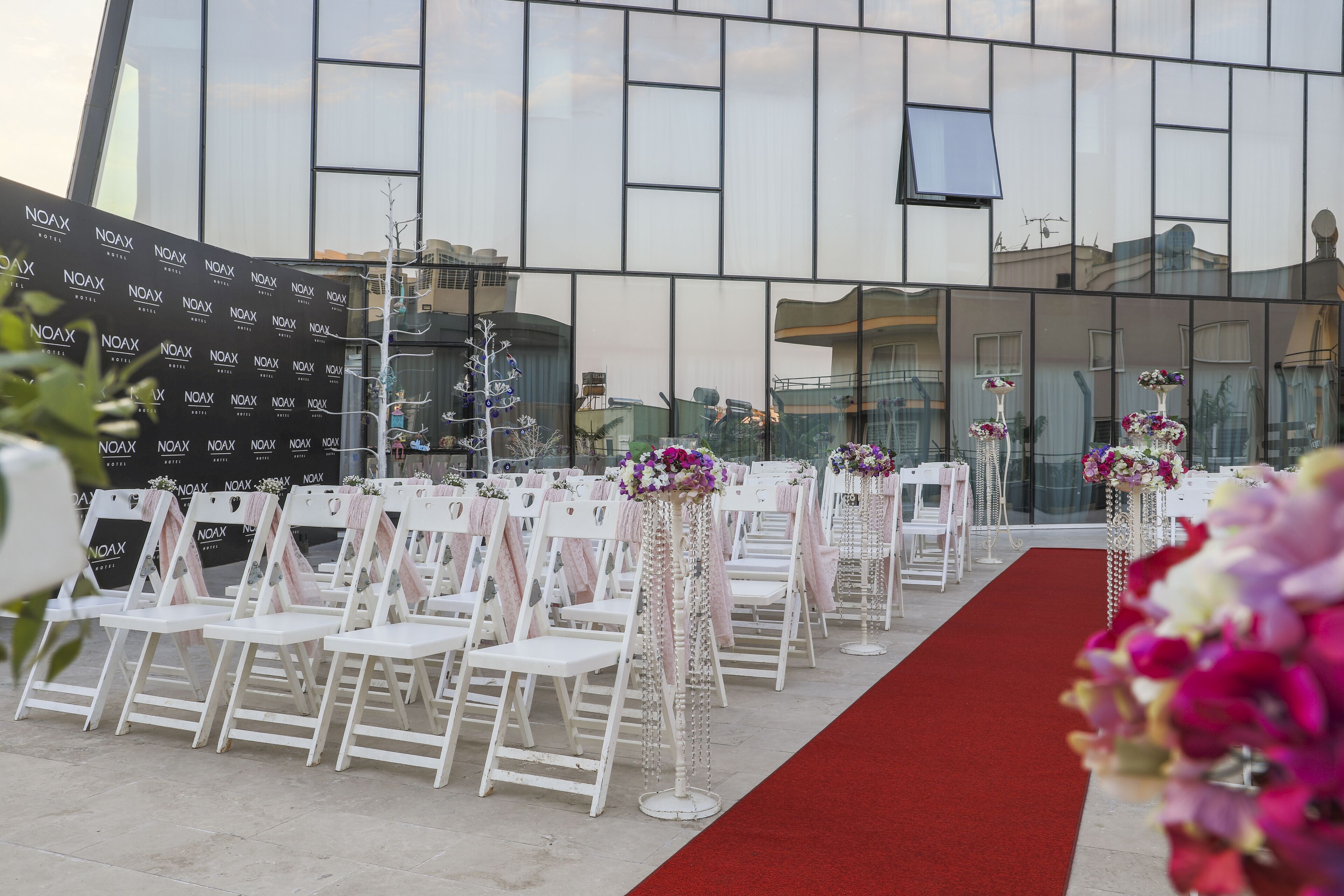 A wedding venue with white chairs and tables, a red carpet, and floral centerpieces.