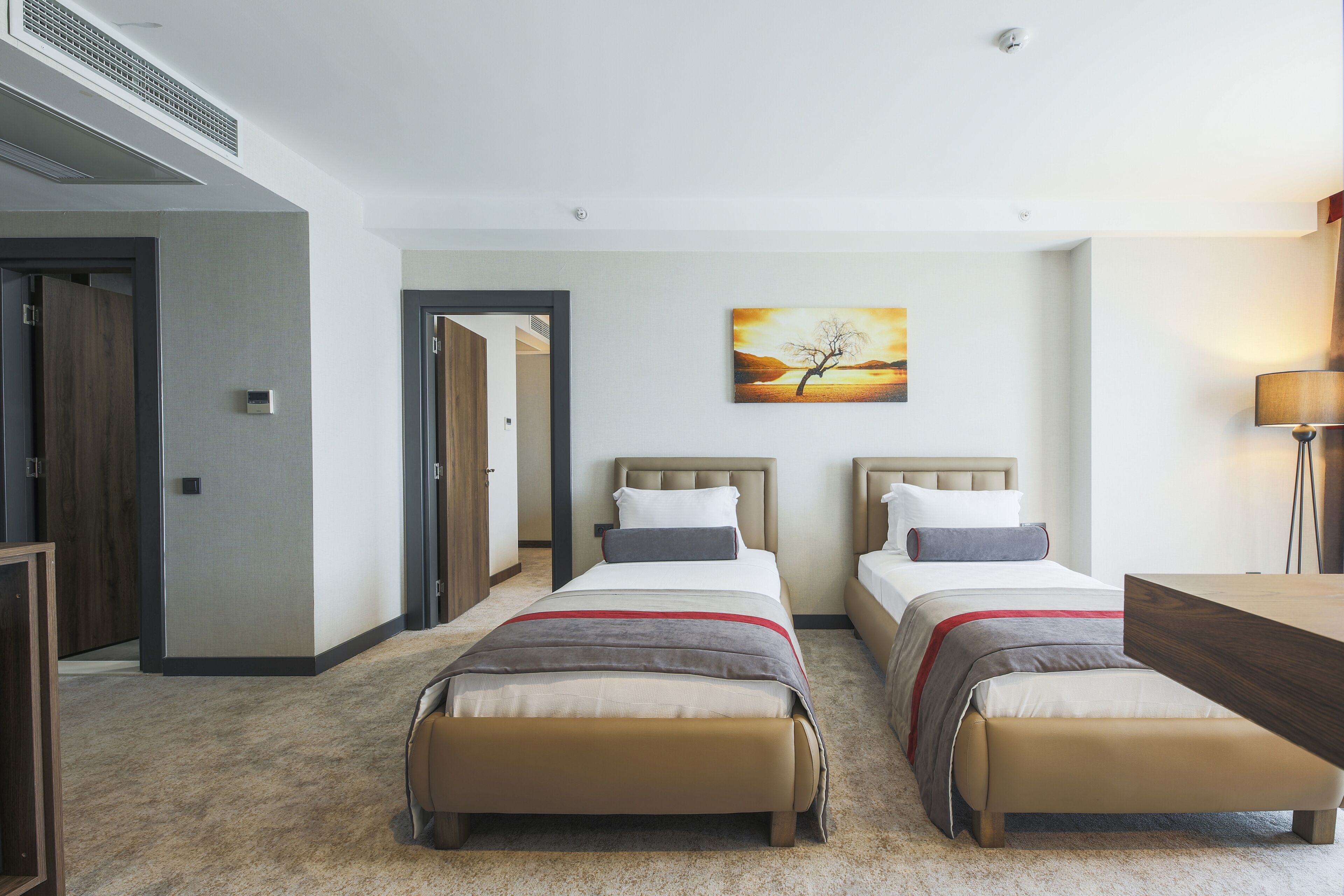 A hotel room with two beds, a painting on the wall, and a desk.