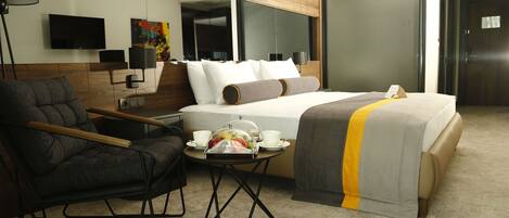 A modern hotel room with a bed, a desk, a chair, a TV, and a painting on the wall.