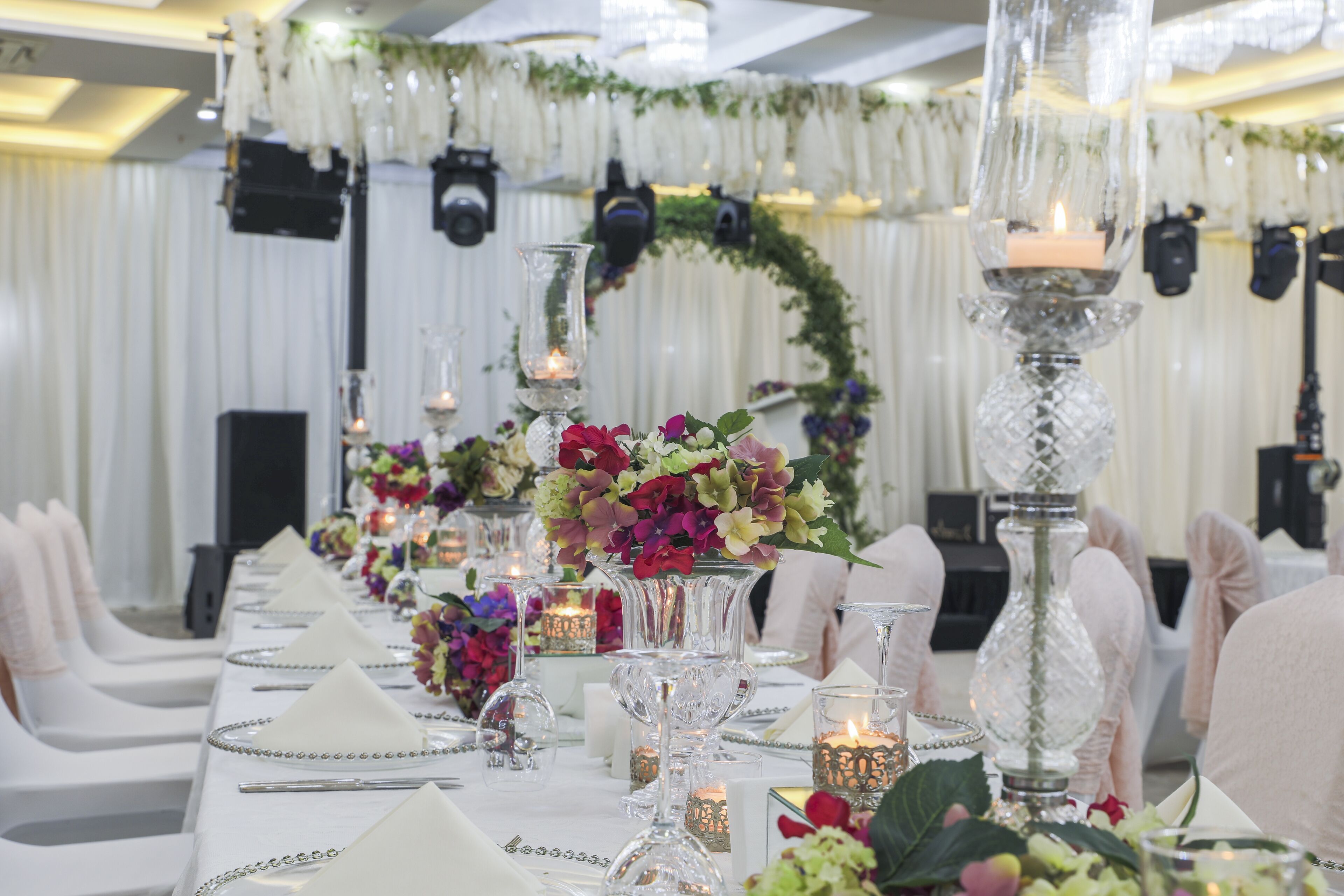 A long banquet table with white tablecloths, glass candle holders, and floral centerpieces.