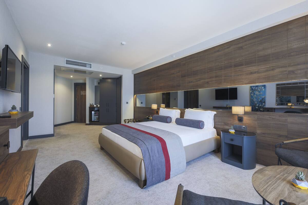 A modern hotel room with a large bed, bedside tables, a desk, and a seating area.