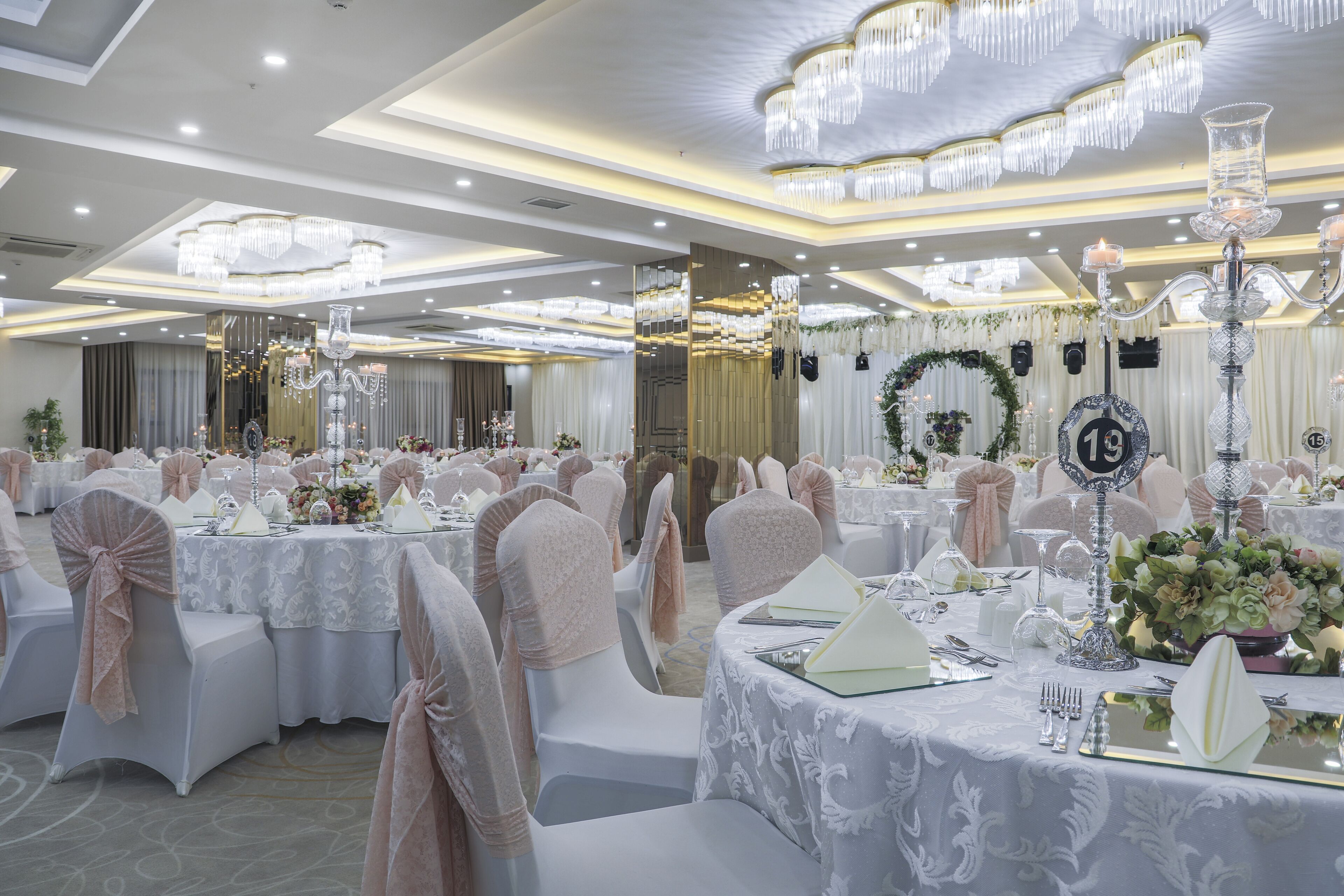 A banquet hall with round tables, white chairs, and chandeliers.