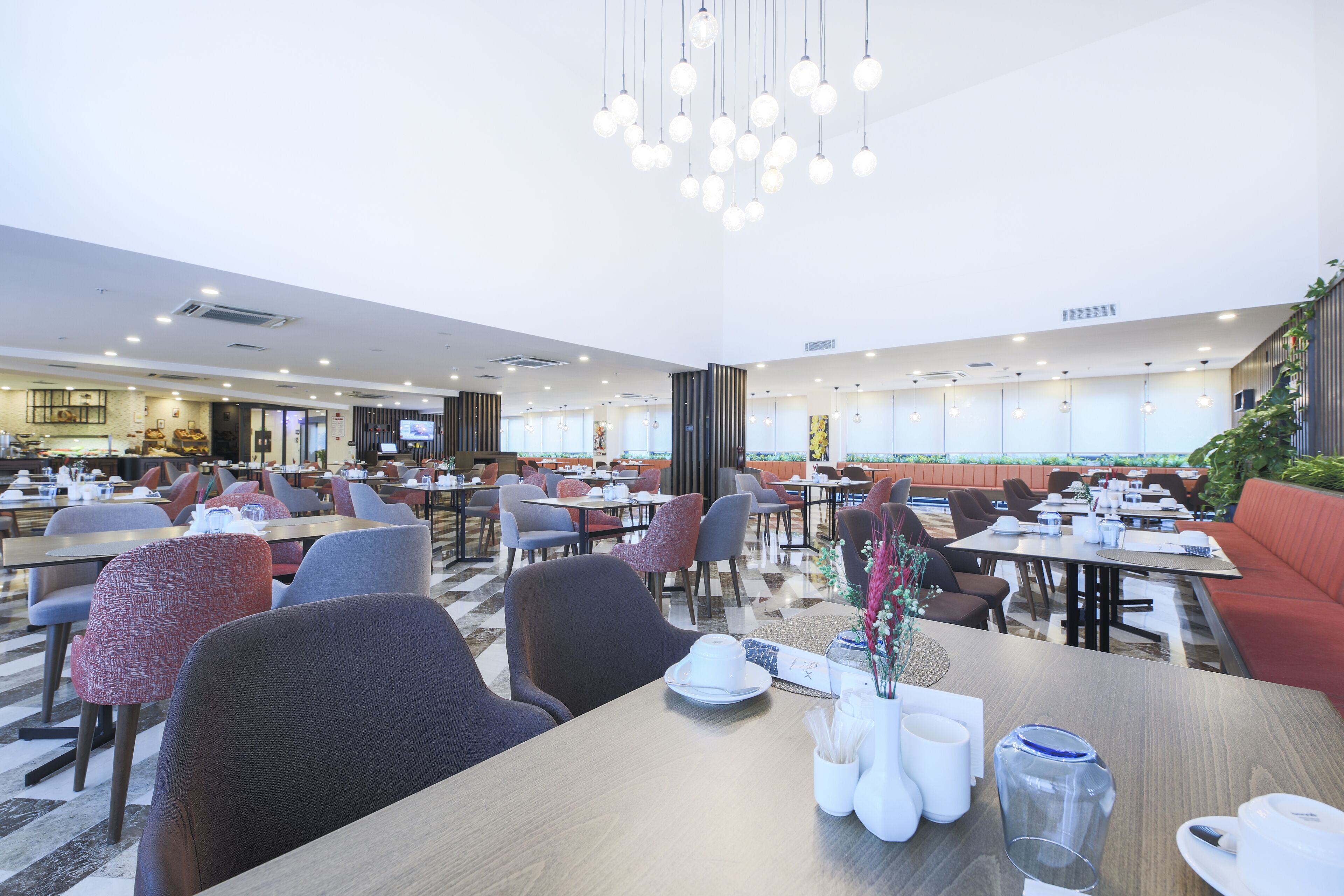 A spacious dining area with multiple tables and chairs, a modern chandelier, and a view of the ocean.