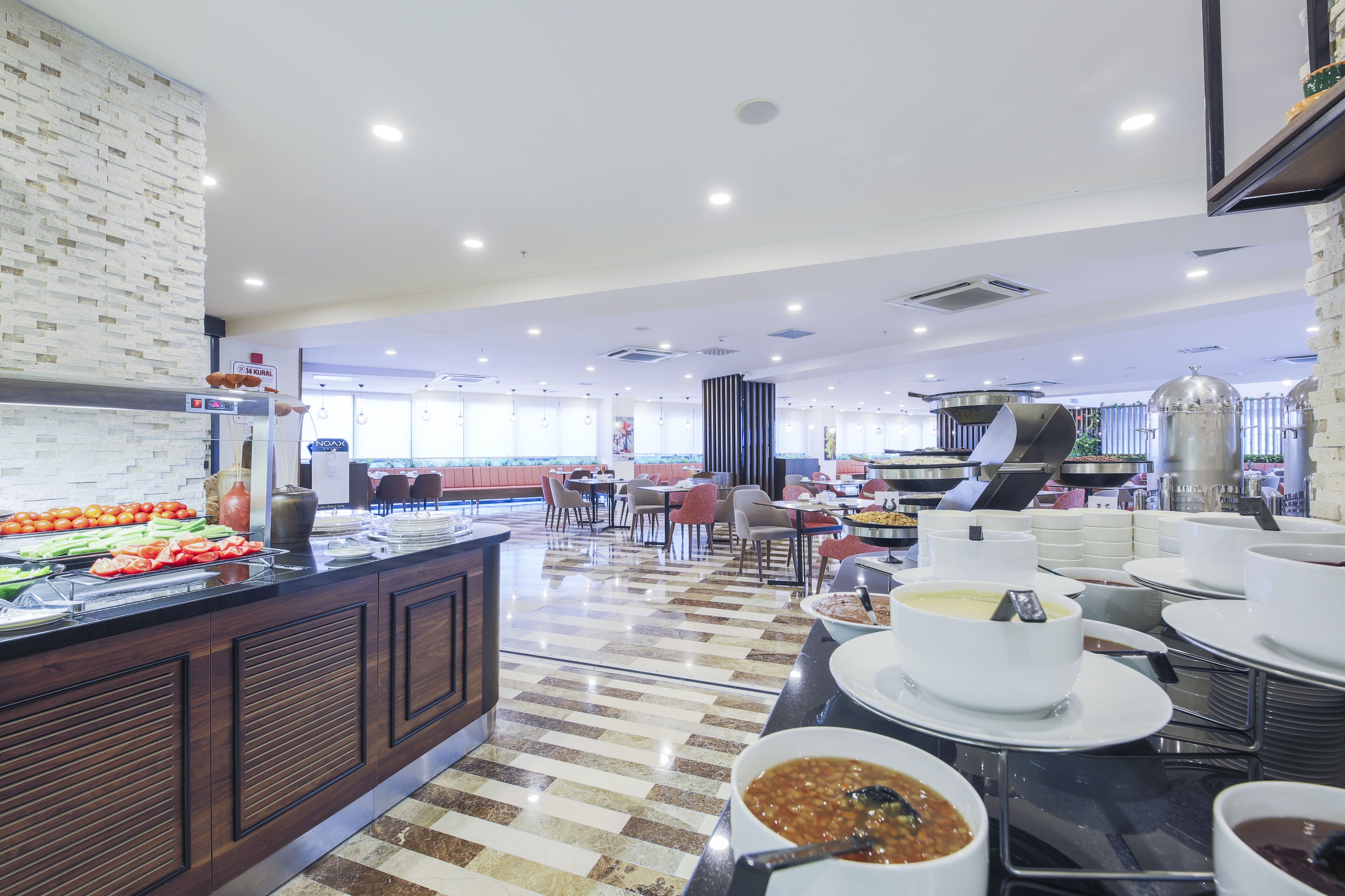 A buffet area with various food options, a seating area with tables and chairs, and a kitchen in the background.