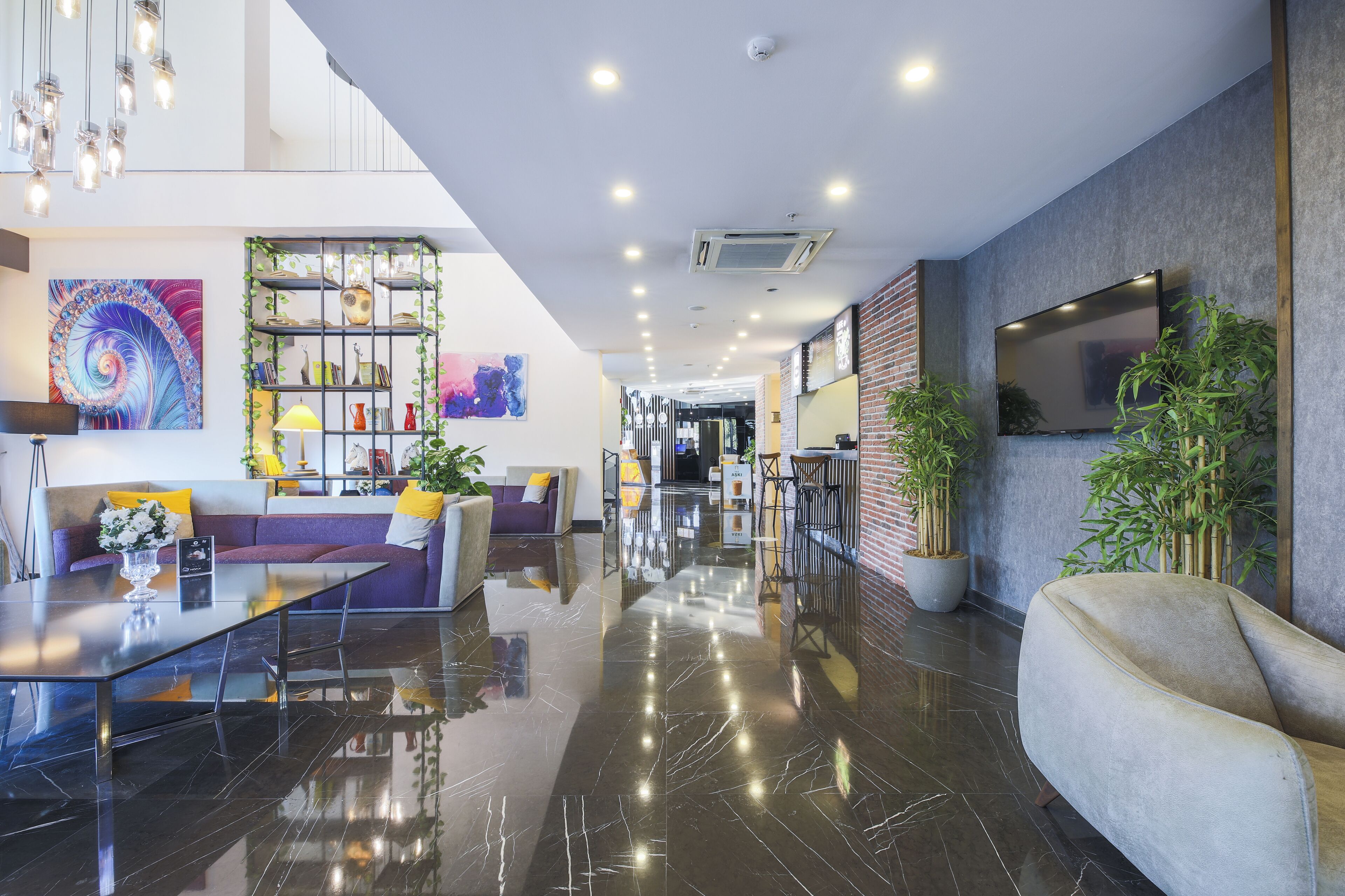 A modern lobby with a polished marble floor, a seating area with a sofa and armchairs, a glass coffee table, and a decorative shelf with plants and books.