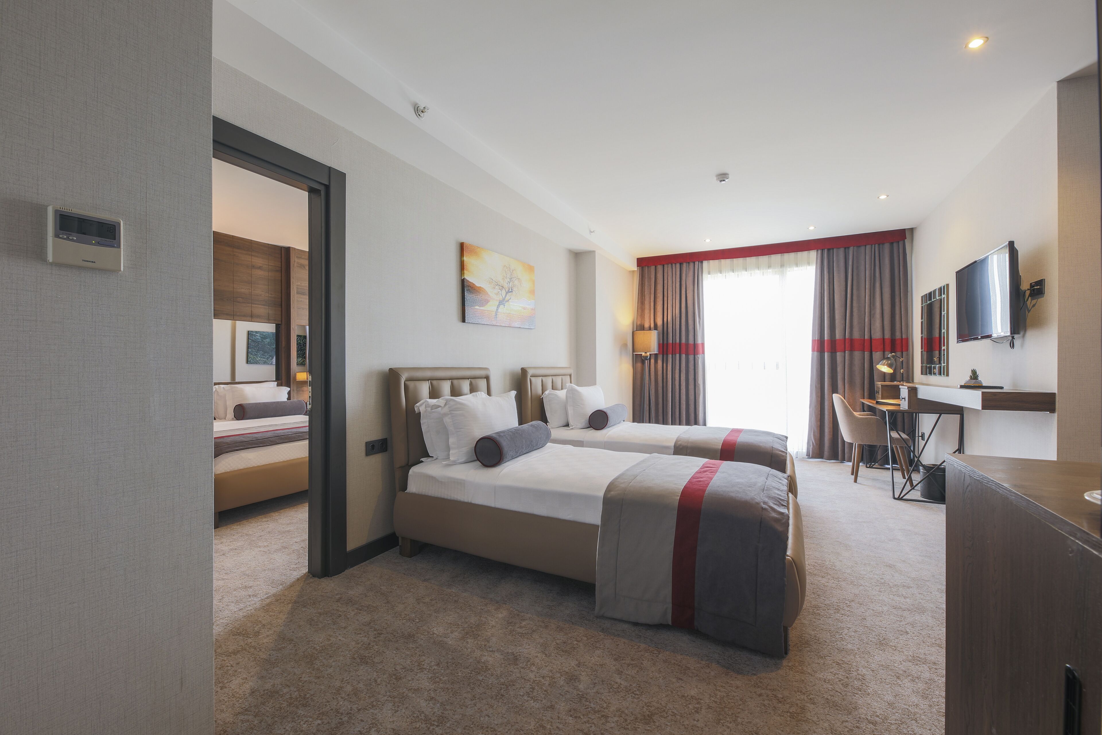 Habitación de hotel con dos camas, un escritorio, una silla, un televisor y un cuadro en la pared.