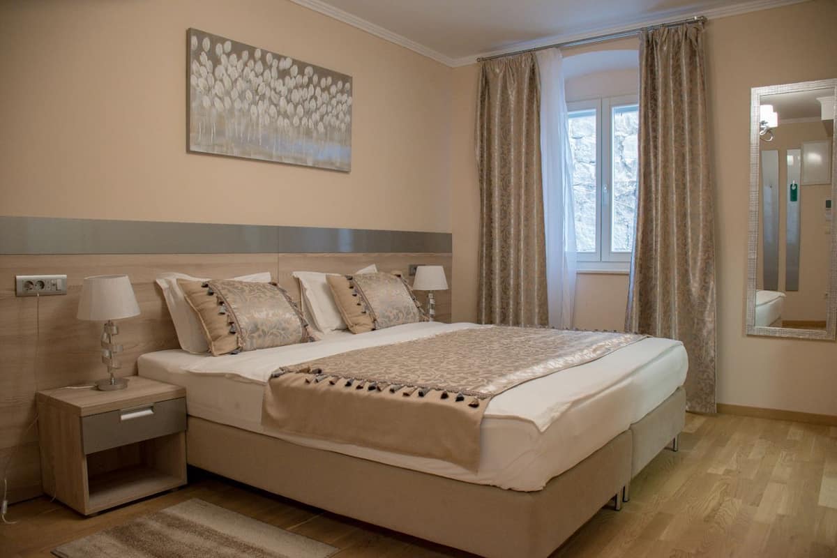 Un dormitorio con una cama grande, dos mesitas de noche, un mueble auxiliar, una ventana con cortinas y una obra de arte colgada en la pared.