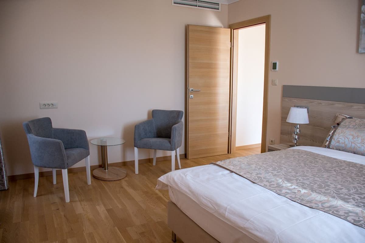 Una habitación de hotel con una cama, dos sillones, una mesita redonda y un armario de madera.