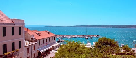 Un pueblo costero con edificios a lo largo de la orilla, un cielo azul despejado y barcos amarrados en un muelle.