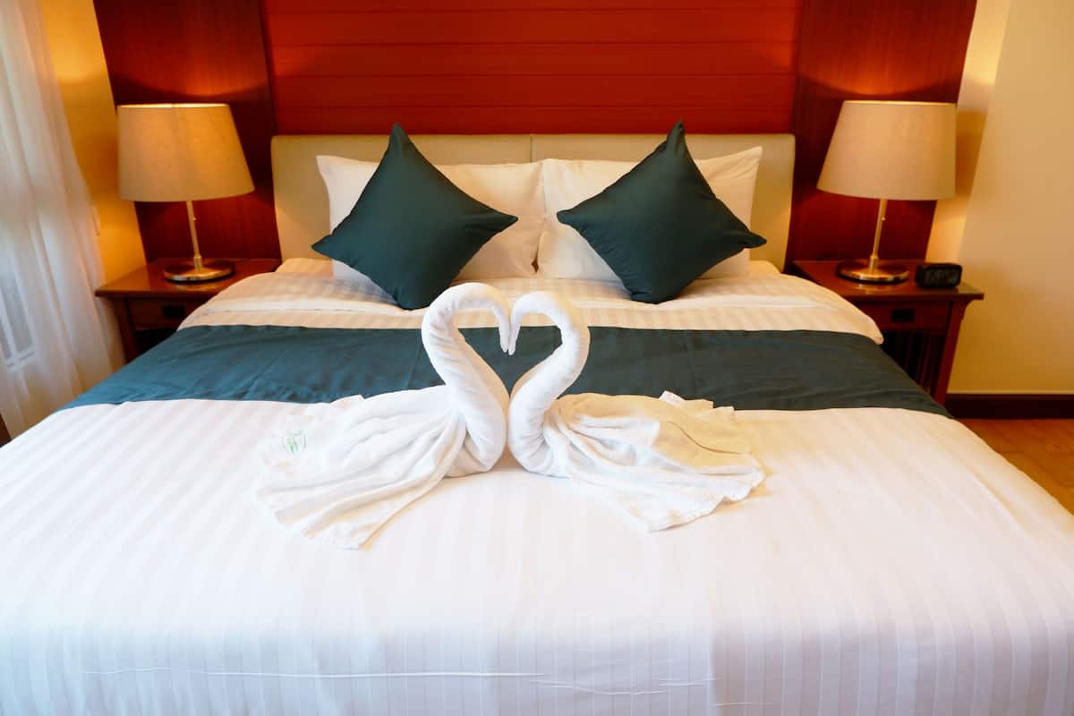 Une chambre d’hôtel avec un lit bien fait, deux oreillers verts et une serviette pliée en forme de cœur.