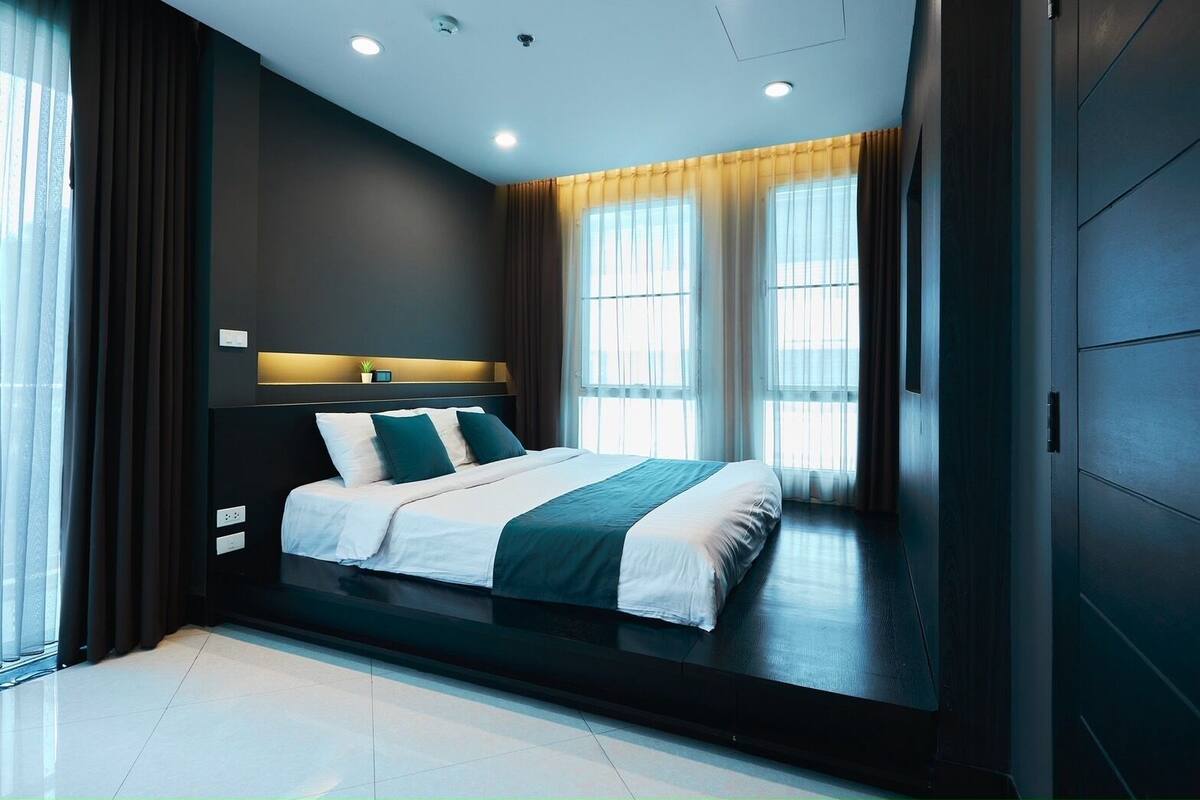Une chambre à coucher moderne avec un grand lit, des murs de couleur sombre et une fenêtre avec des rideaux.