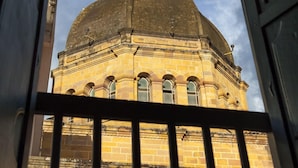 Une vue d’un bâtiment doté d’un dôme et de fenêtres en arc de cercle, prise à travers une porte surmontée d’une rambarde en métal.