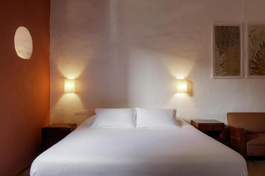 Una habitación de hotel con una cama grande, dos mesitas de noche y una silla.