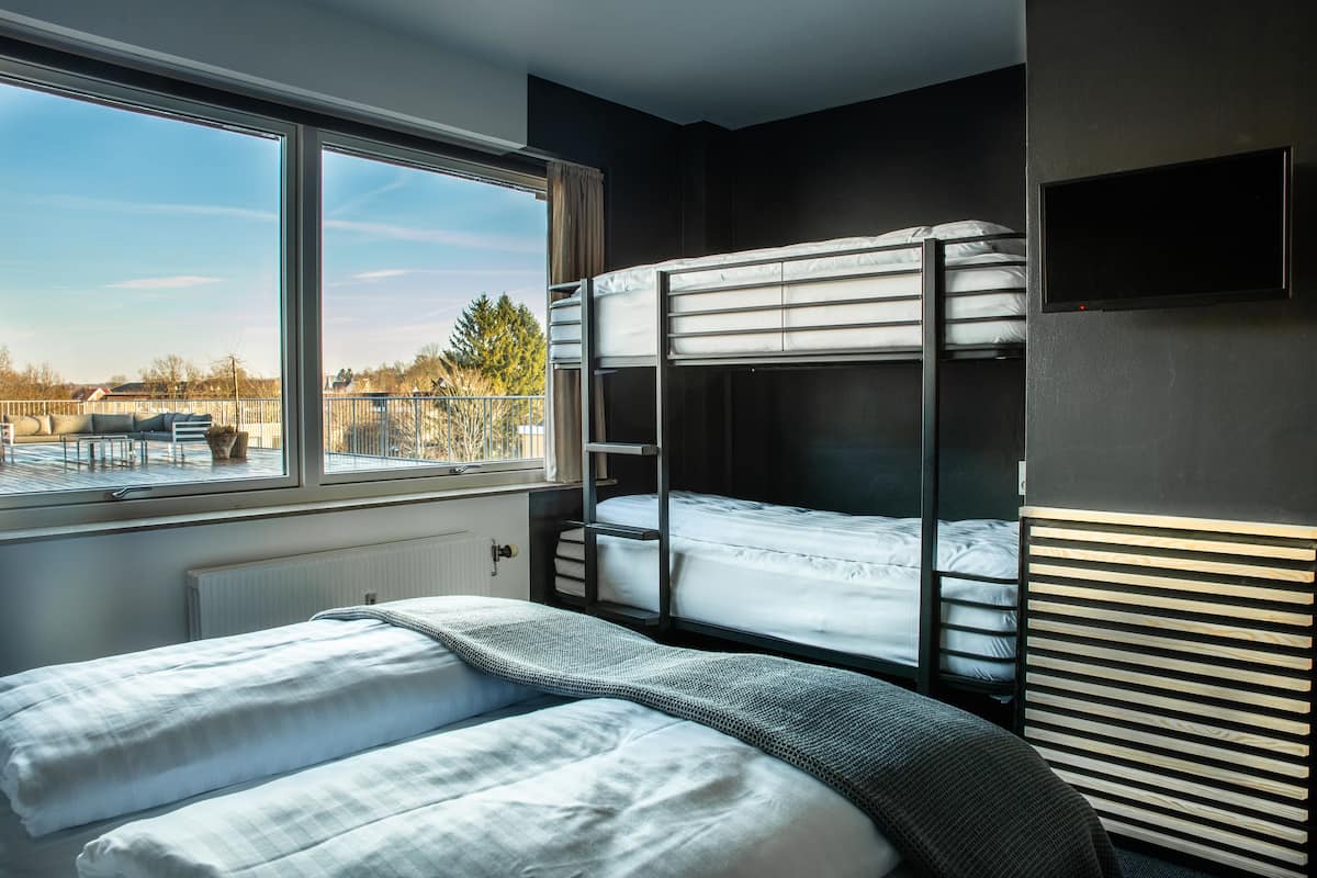 A bunk bed room with a large window, a radiator, and a TV mounted on the wall.