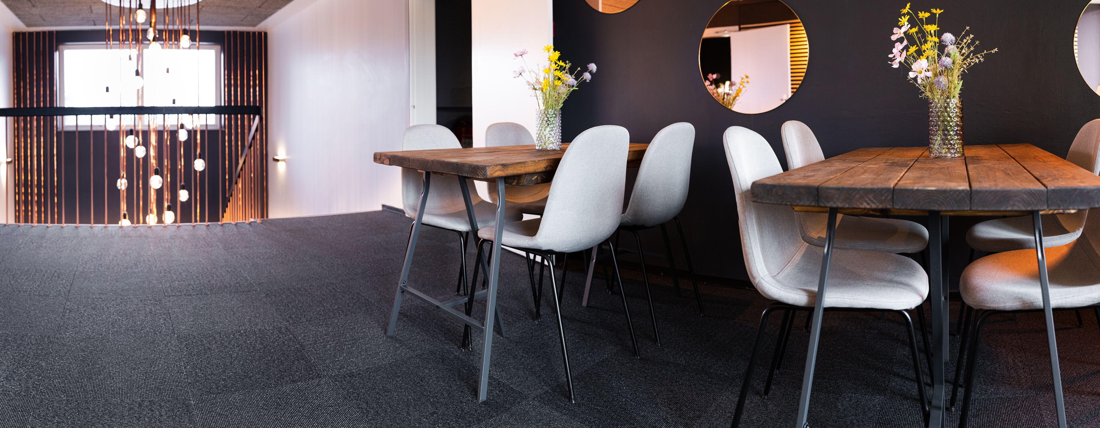 A modern conference room with a wooden table, grey upholstered chairs, and a vase of flowers.