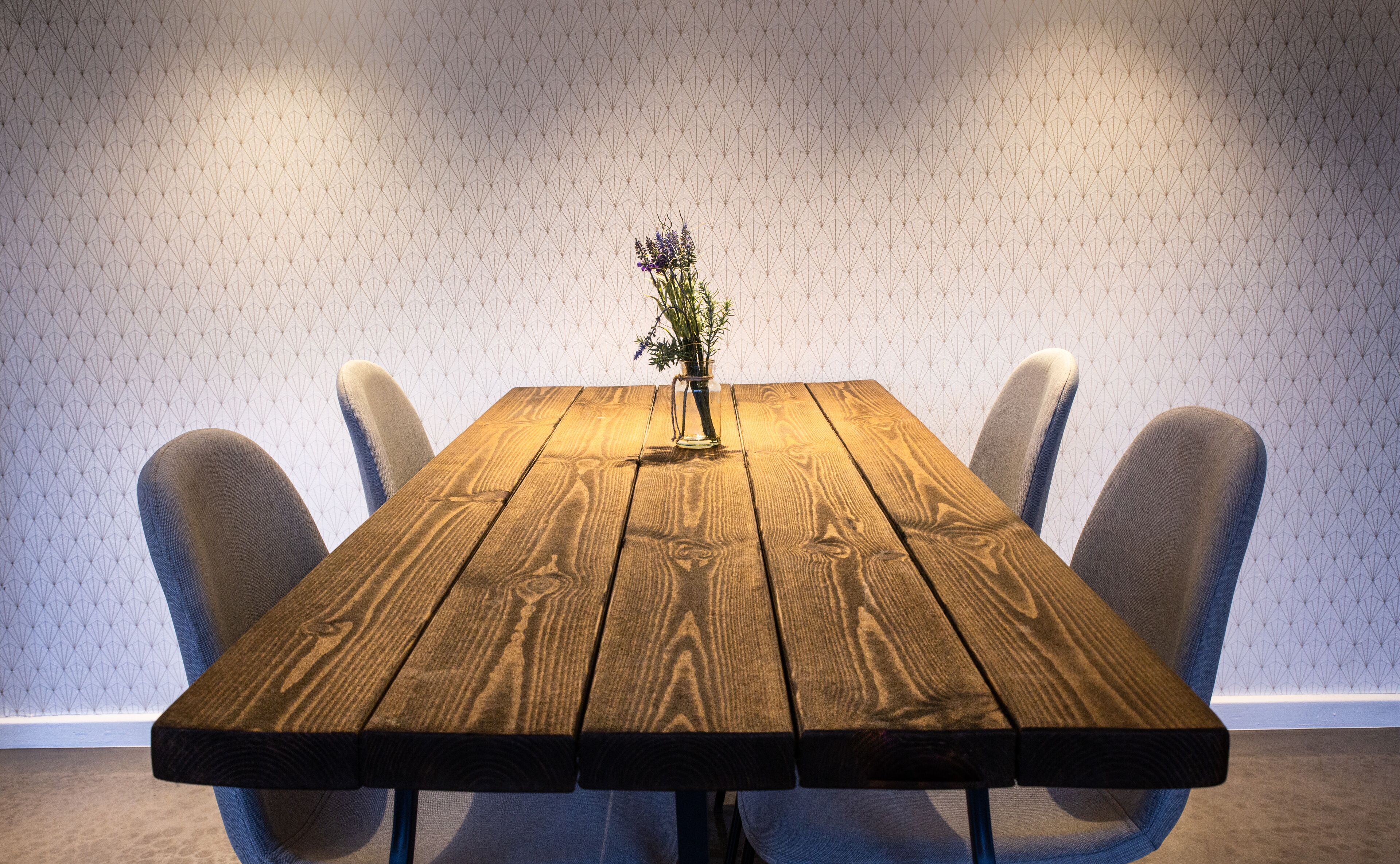 A wooden table with a vase of flowers in the center, surrounded by chairs.