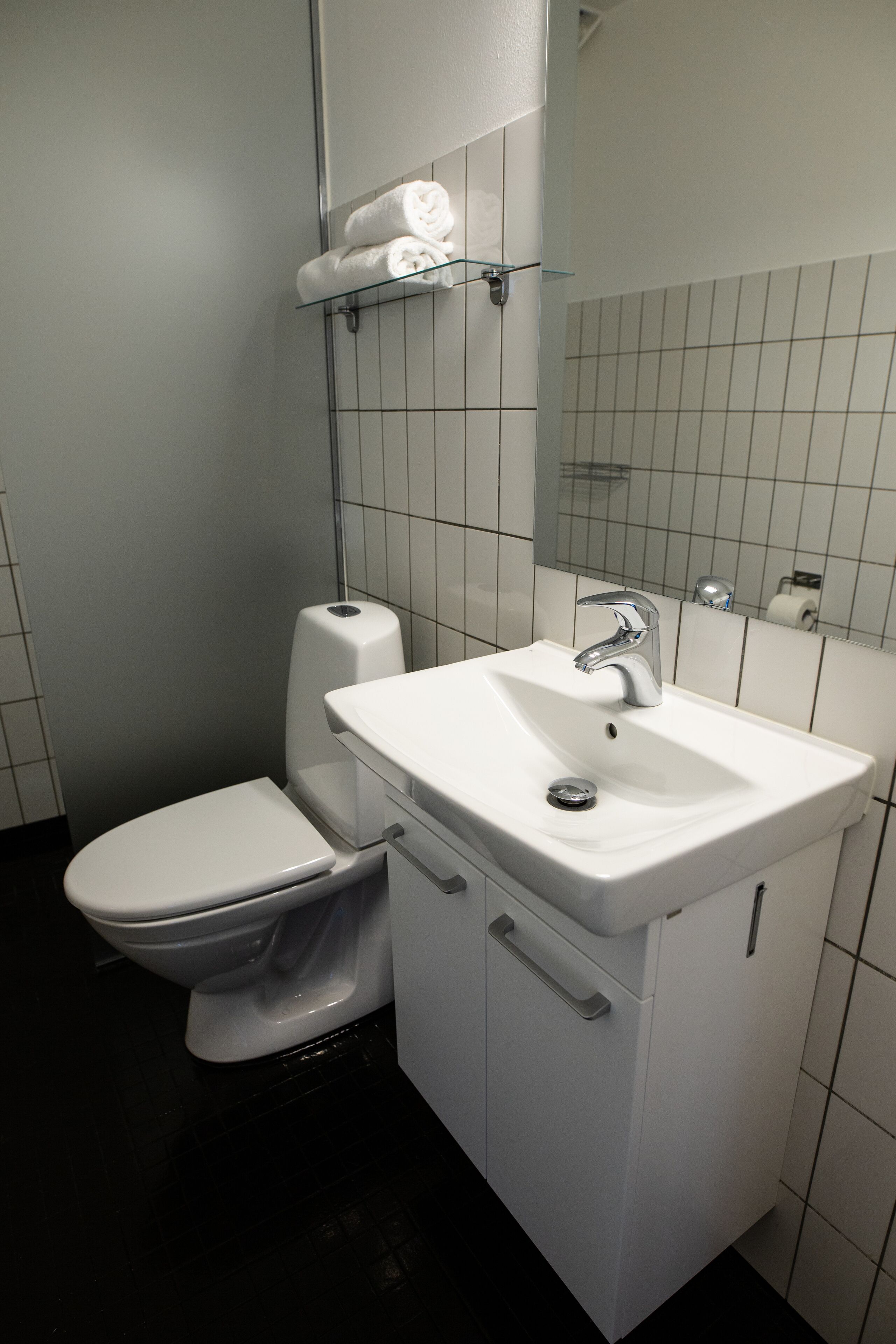 Un baño con inodoro y lavamanos blancos, y un espejo sobre el lavamanos.