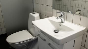 Un baño con inodoro y lavamanos blancos, y un espejo sobre el lavamanos.
