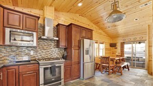 A wooden cabin kitchen with a stone tile floor, a stainless steel refrigerator, and a wooden dining table with benches. - Circle Views #1602 (Big Bear Lake)