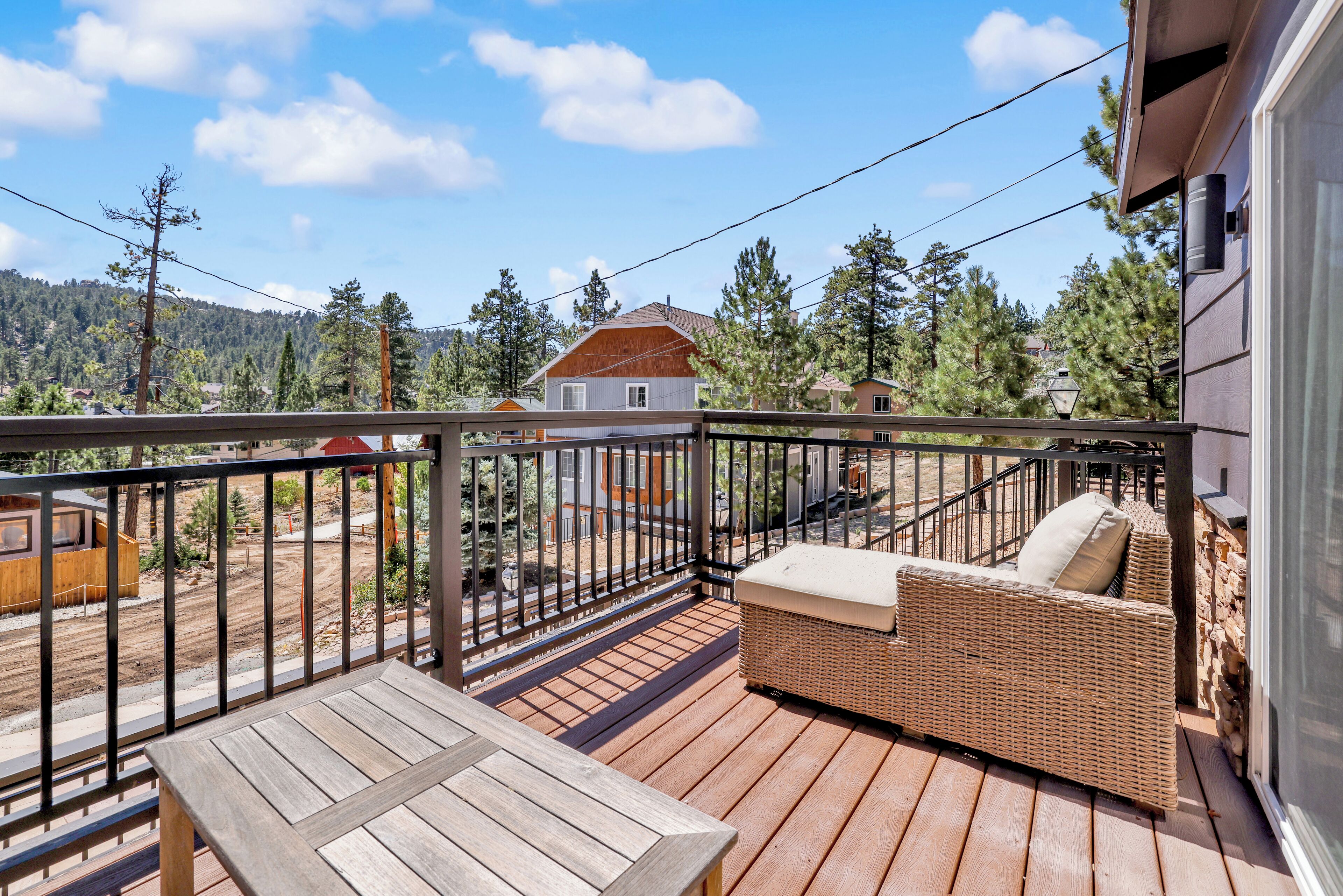 A wooden deck with a wicker sofa and a table, overlooking a residential area with houses and trees.