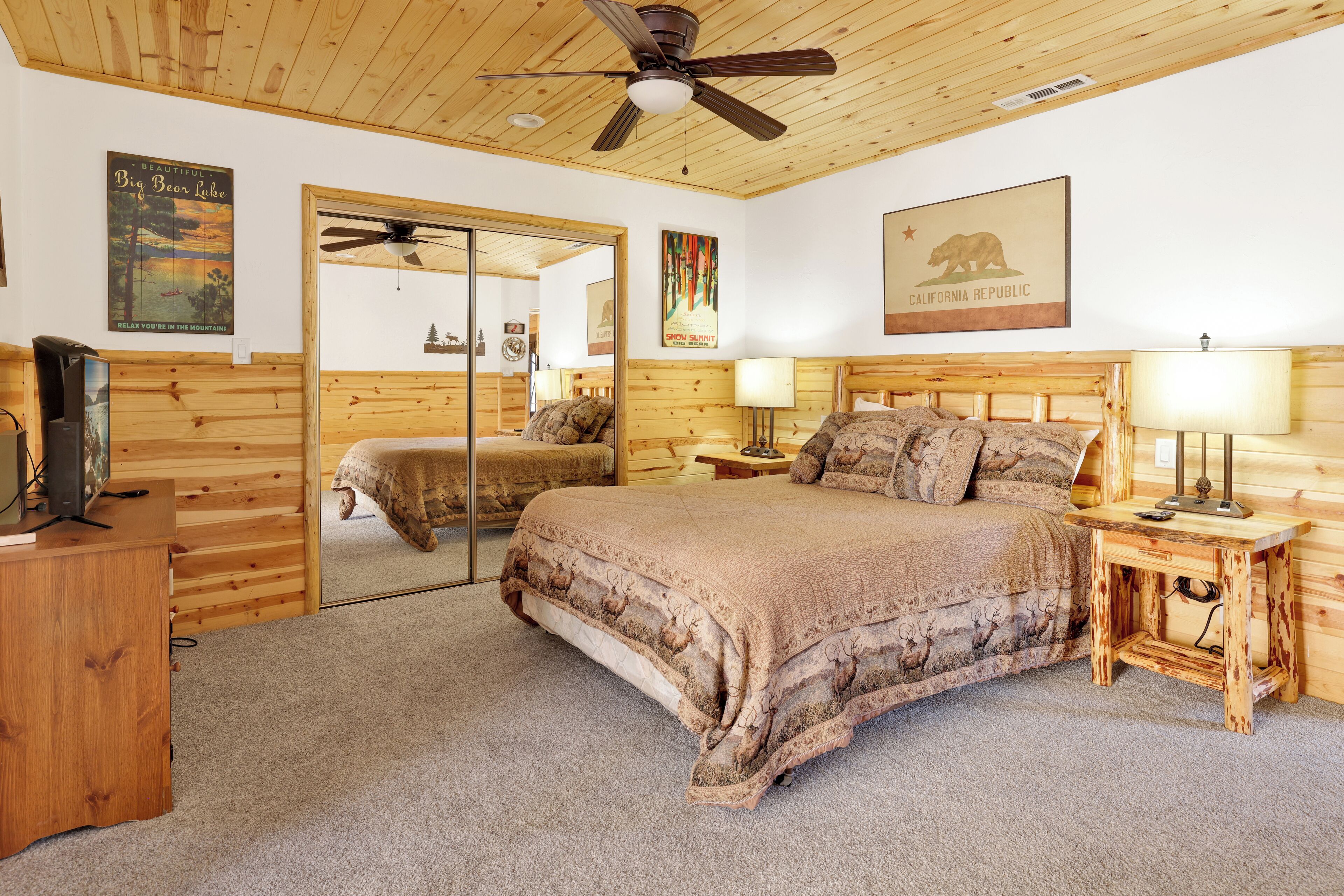 A bedroom with a large bed, wooden headboard, a ceiling fan, and a California Republic poster.