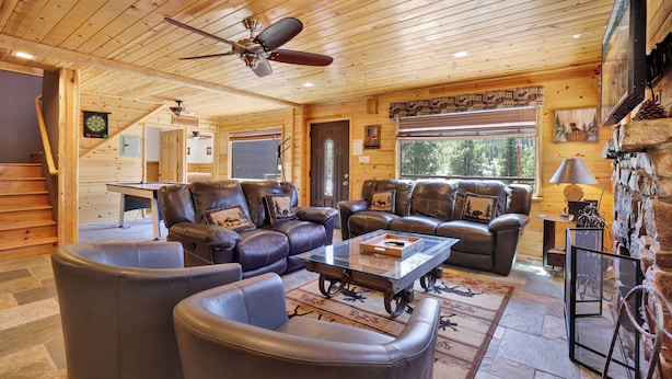 A log cabin interior with leather sofas, a glass coffee table, a fireplace, and a ceiling fan. - Circle Views #1602 (Big Bear Lake)
