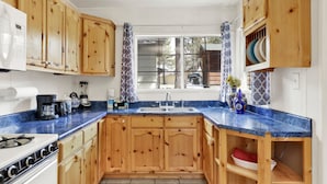 Une cuisine avec des meubles de rangement en bois, un plan de travail bleu, une cuisinière, un évier et une fenêtre avec des rideaux.
