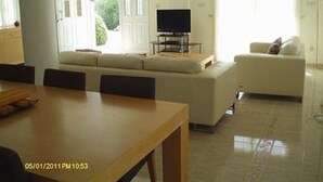 A modern living room with a sofa, a television, and a dining area with a table. - 3 Bed Villa 10 Minutes Drive From Beautiful Beach (Chlorakas)