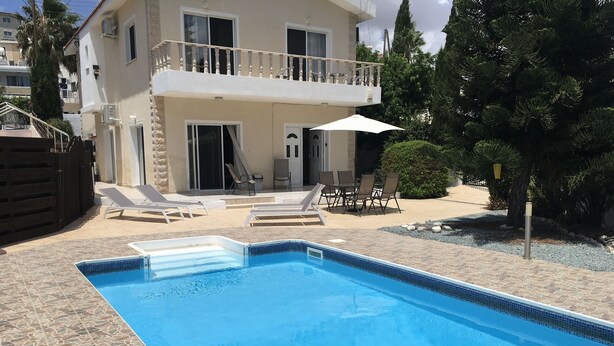 A swimming pool with lounge chairs and a table, surrounded by a stone patio and a building with a balcony. - 3 Bed Villa 10 Minutes Drive From Beautiful Beach (Chlorakas)