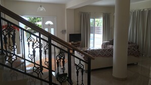 A spacious living area with a staircase, a sofa, a television, and a large window with curtains. - 3 Bed Villa 10 Minutes Drive From Beautiful Beach (Chlorakas)