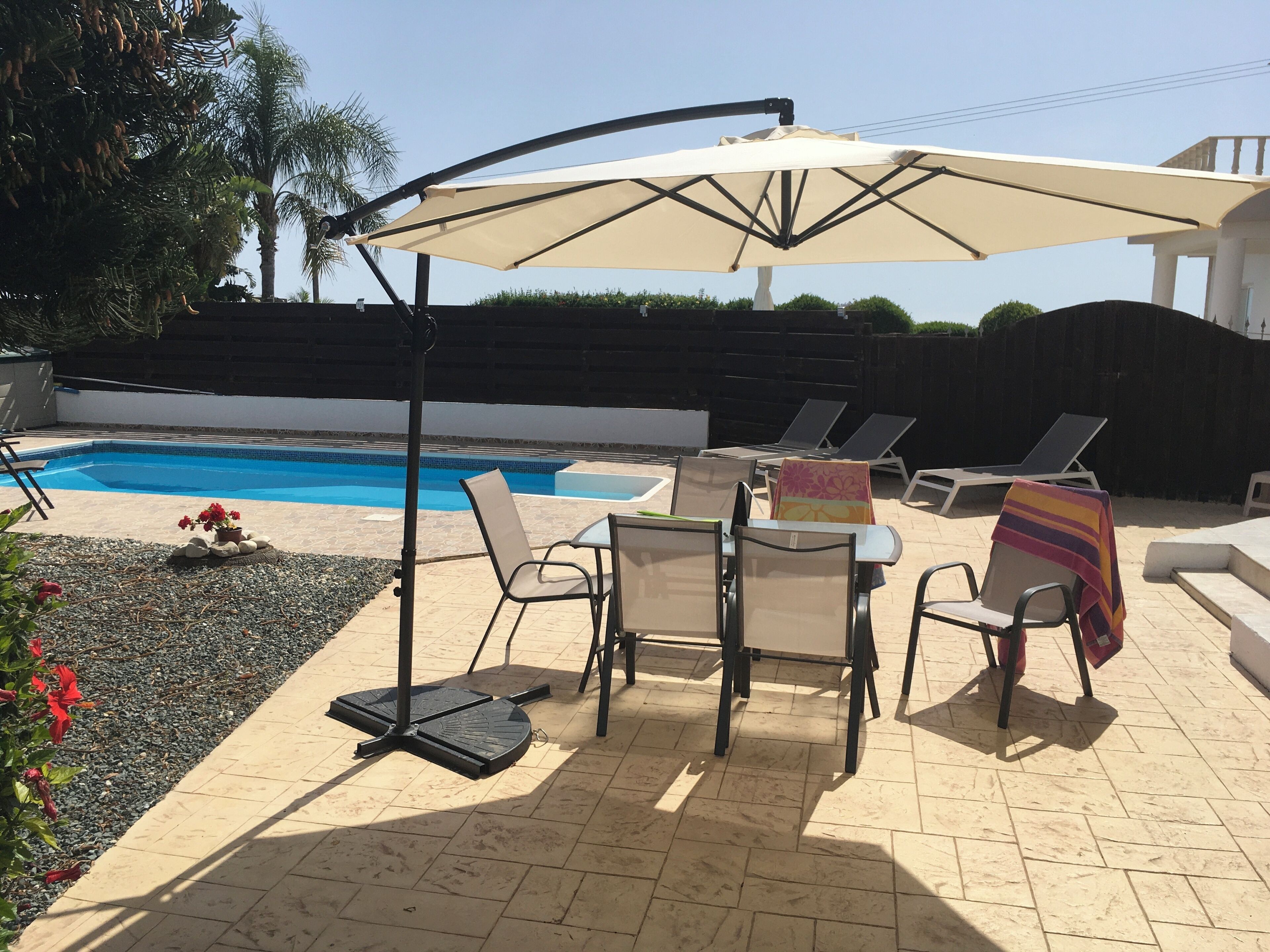 Zona junto a la piscina con sillones reclinables, una mesa y una sombrilla.