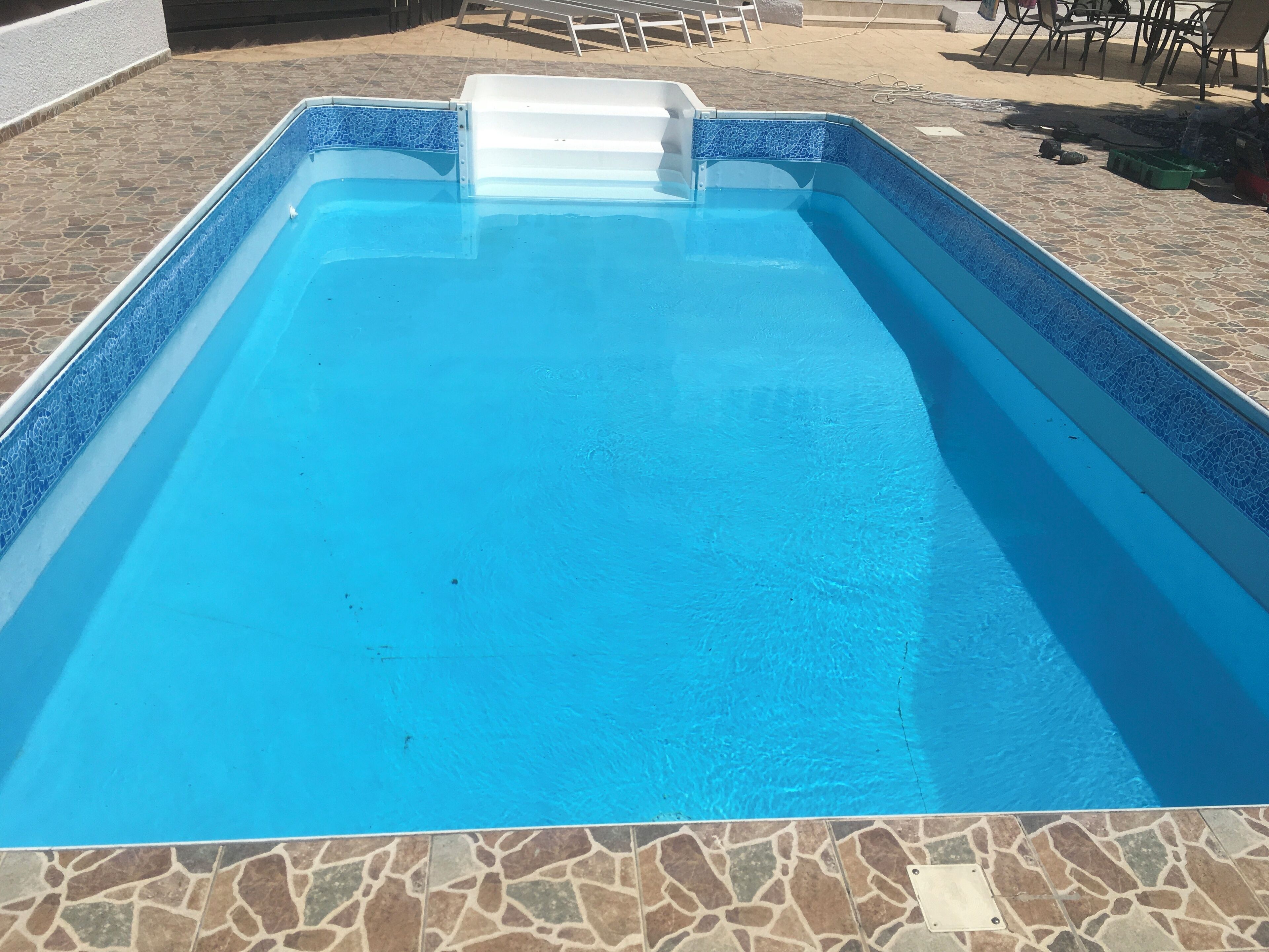A rectangular swimming pool with a blue mosaic border and a stone-tiled deck surrounding it.