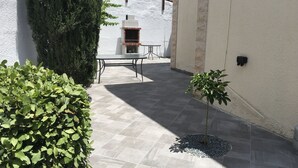 An outdoor patio area with a stone floor, a table and chairs, a small tree, and a white wall with a brick fireplace. - 3 Bed Villa 10 Minutes Drive From Beautiful Beach (Chlorakas)