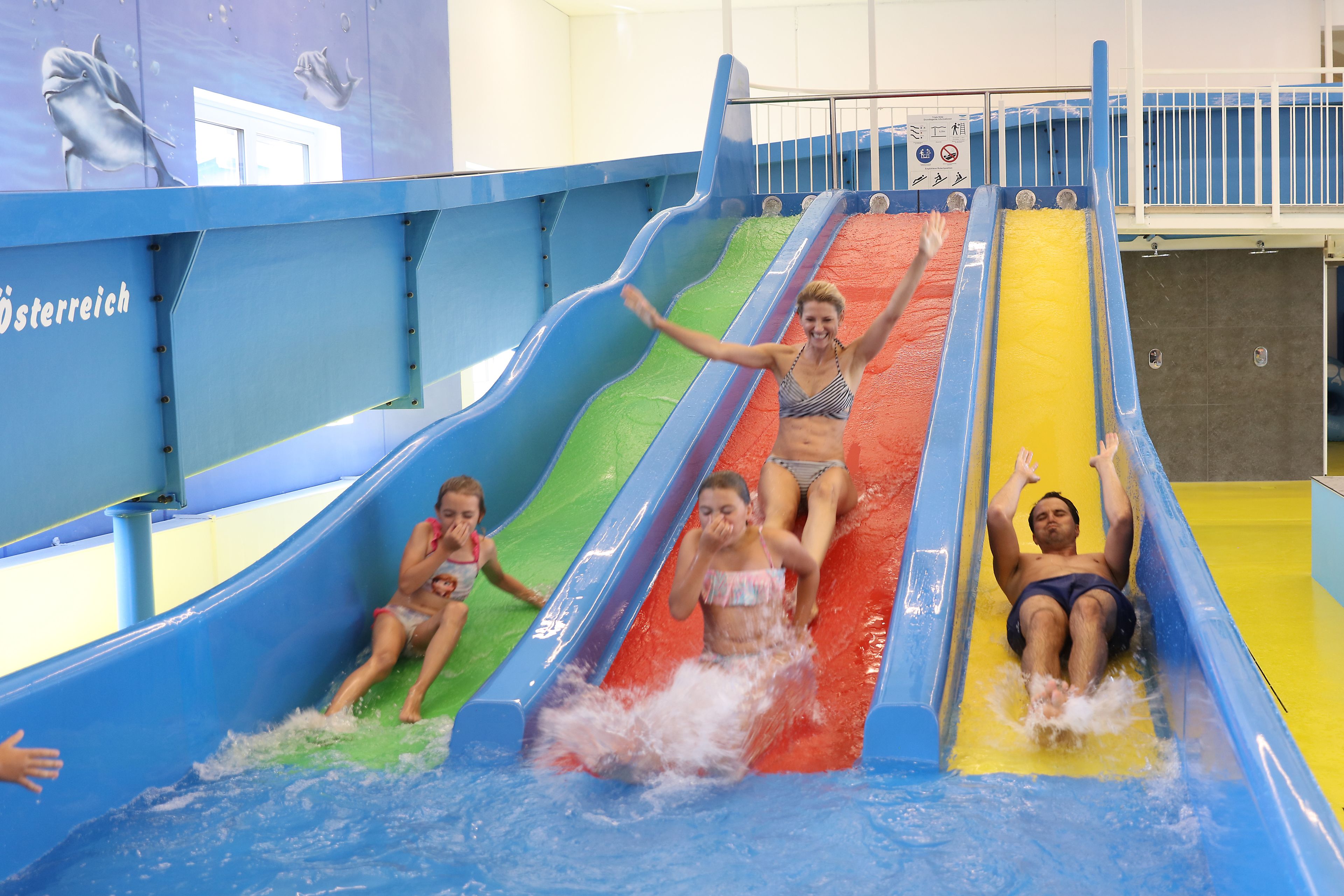 A water slide with multiple lanes and a dolphin mural on the wall.