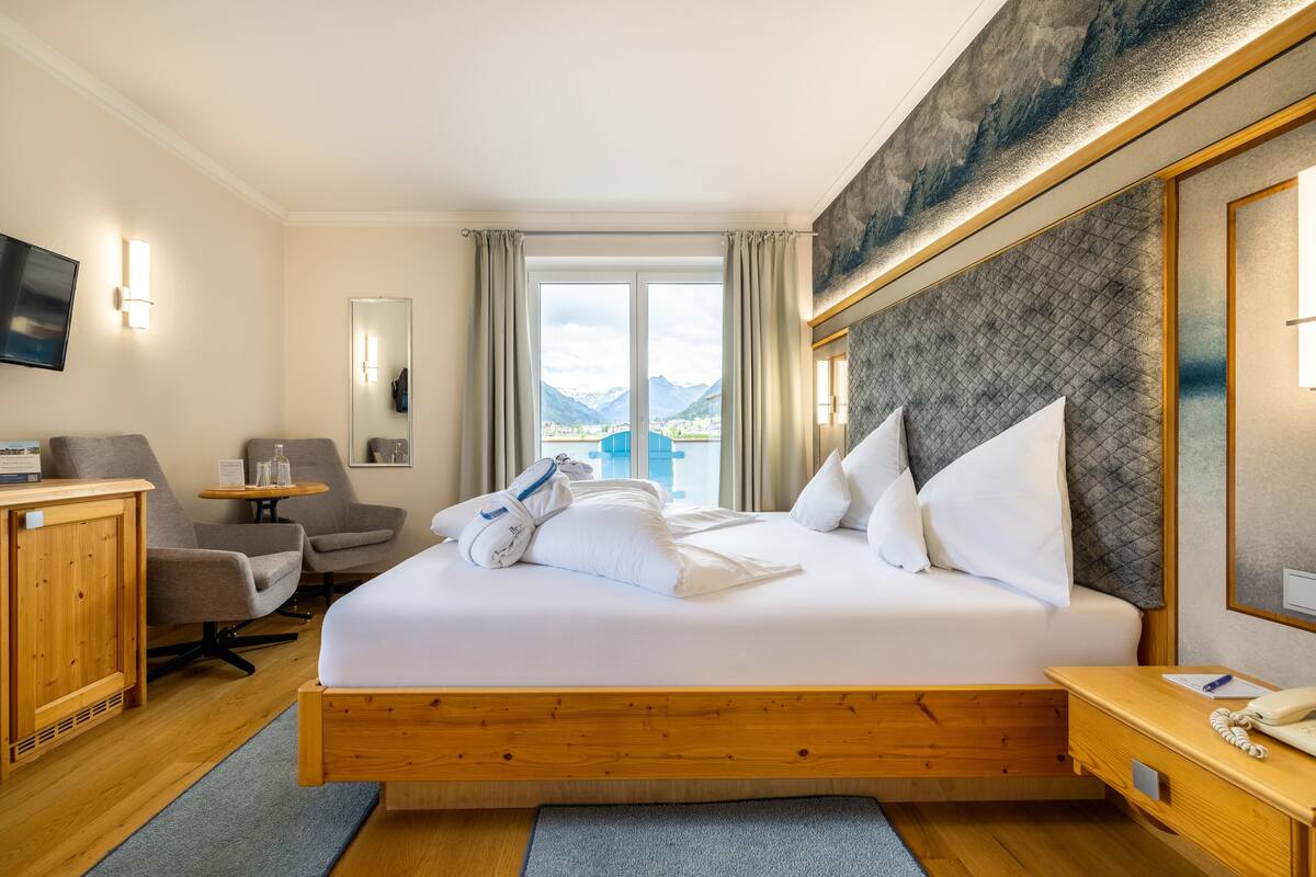 Une chambre d’hôtel avec un grand lit, un bureau, une chaise, une télévision et une vue sur les montagnes par la fenêtre.