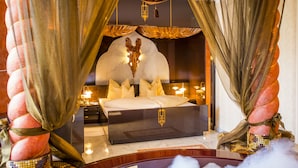 Un dormitorio lujoso con una cama grande, cortinas ornamentadas y un cabecero decorativo.