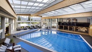 Una piscina interior con techo de vidrio, sillas de descanso y zona de bar.