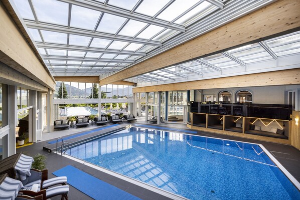 Una piscina interior con techo de vidrio, sillas de descanso y zona de bar.