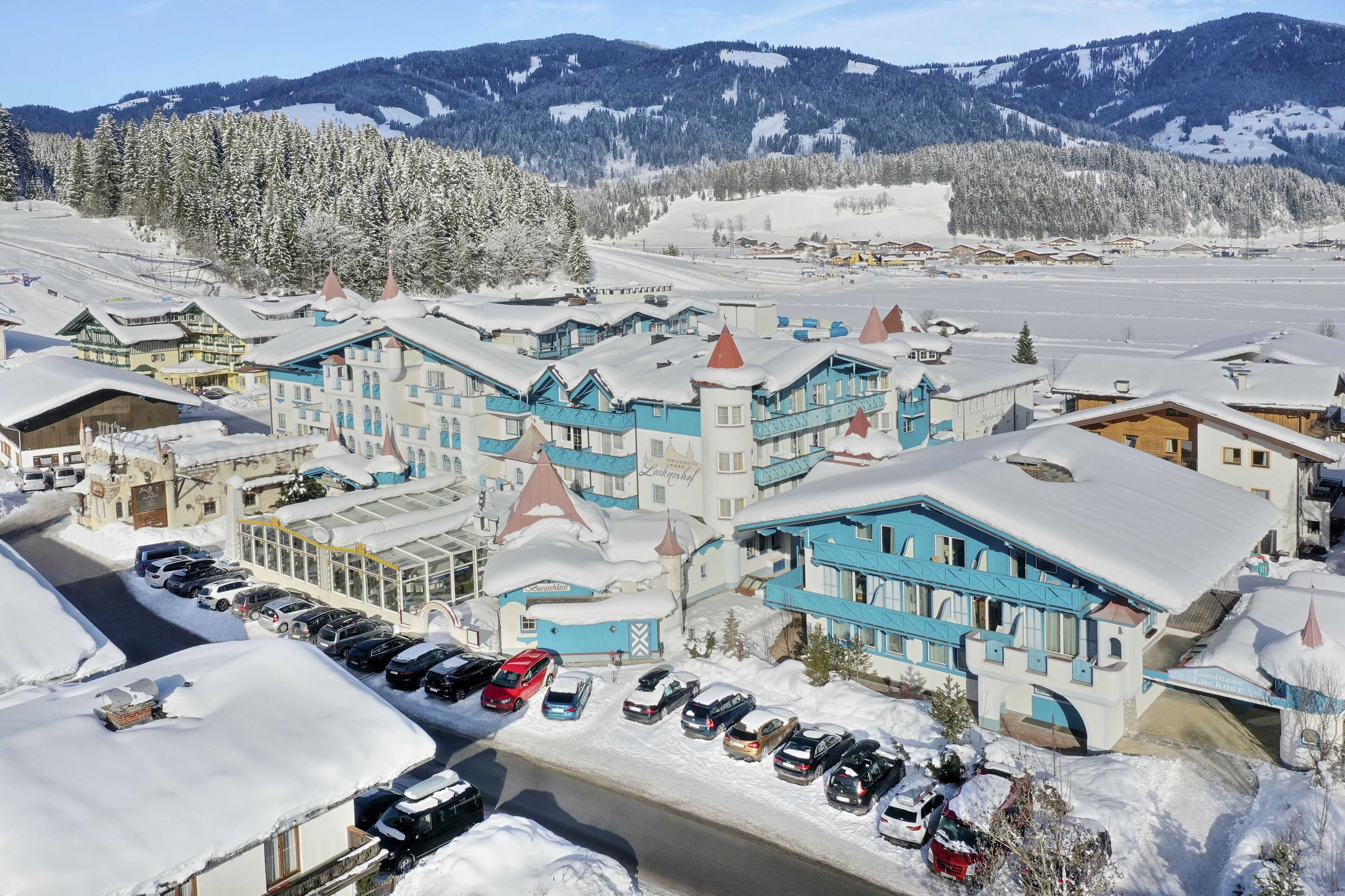 Un hotel cubierto de nieve con varias edificaciones, un estacionamiento y un paisaje montañoso.