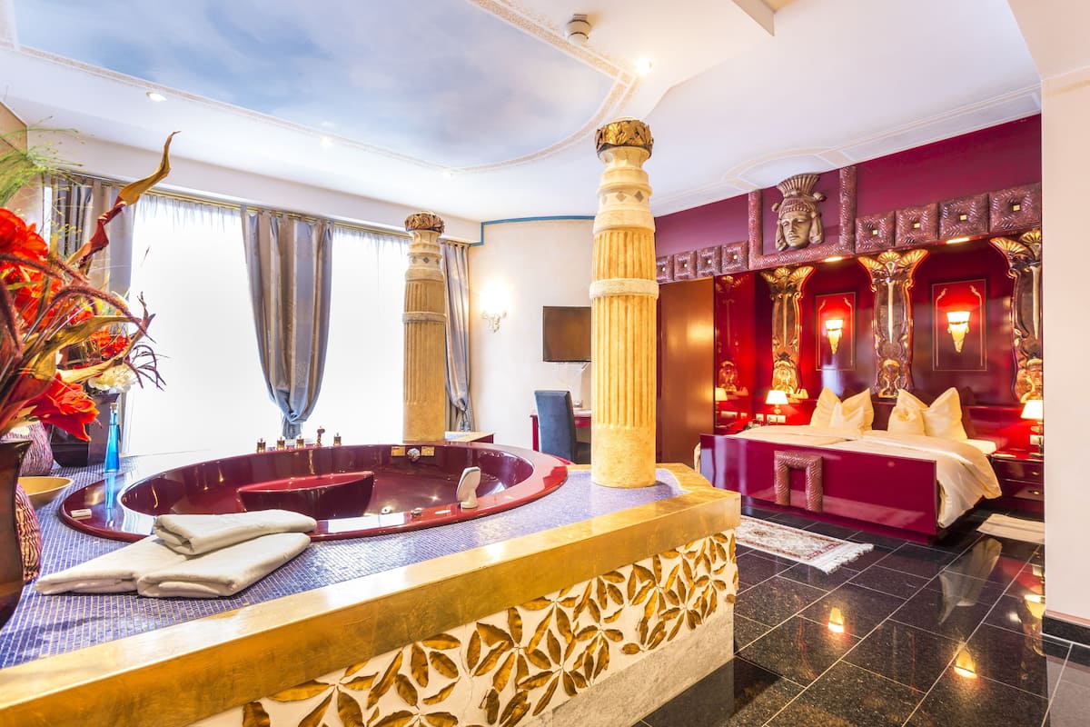 Une chambre d’hôtel luxueuse, dotée d’une grande baignoire, d’un lit moelleux et de colonnes décoratives.