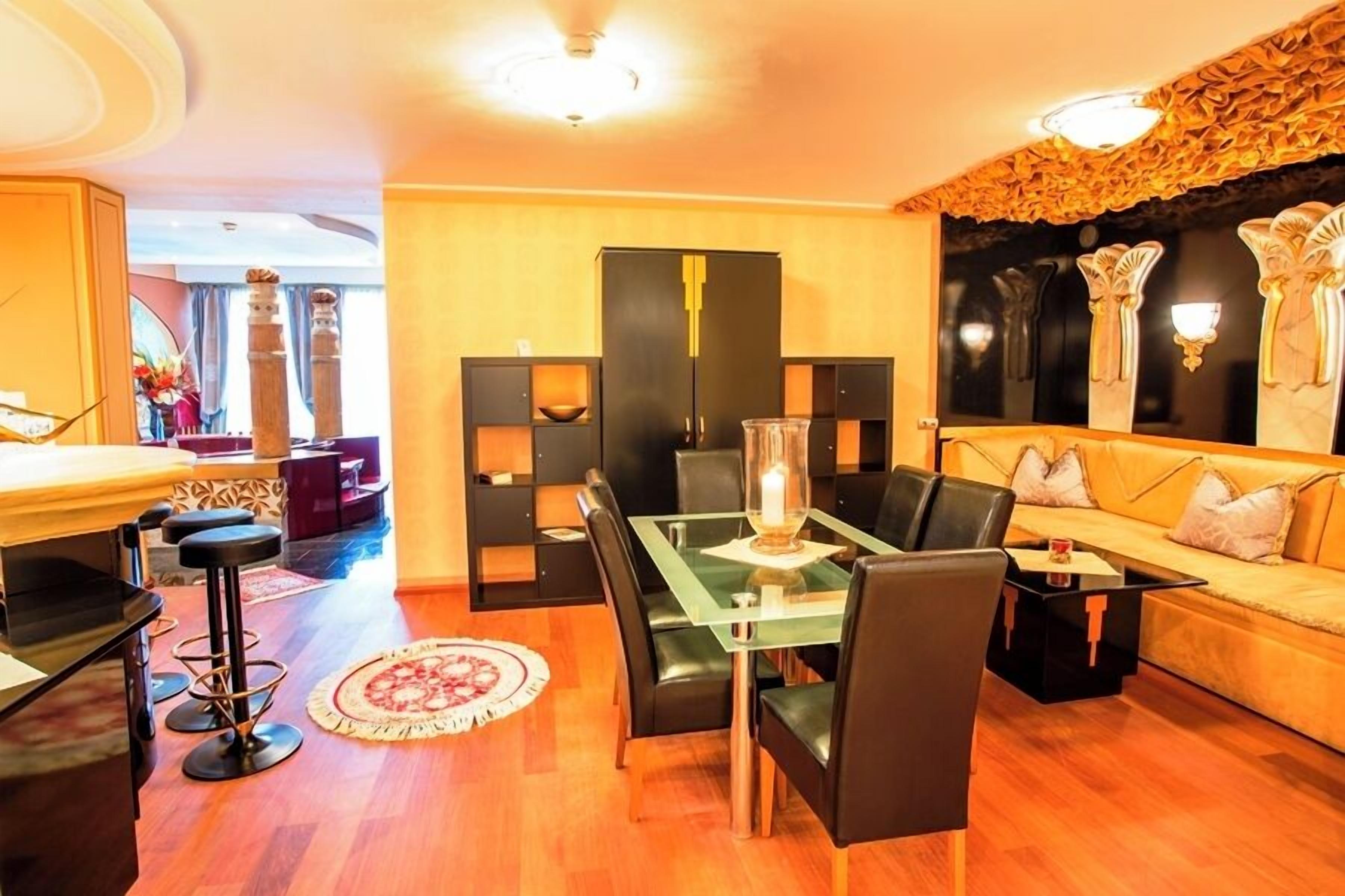 Una sala de estar moderna con una mesa de comedor de vidrio, sillas negras, un sofá y una pared decorativa con un espejo.