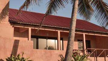 A building with a red roof and pink walls, featuring large windows and a palm tree in the foreground.
