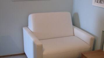 Une pièce avec un canapé blanc, une chaise en bois et une petite table en bois.