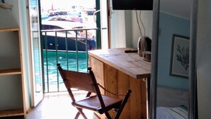 A room with a wooden desk, a chair, a TV, and a bed with a striped pillow. - La Calata (Portovenere)