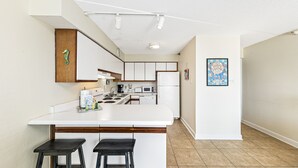A modern kitchen with white cabinetry, a central island with stools, a microwave, and a refrigerator. - Emerald Skye 54 (Orange Beach)