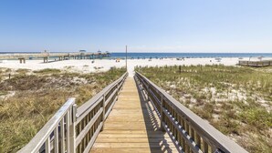 A wooden boardwalk leading to a beach with a pier and beach umbrellas. - Emerald Skye 54 (Orange Beach)