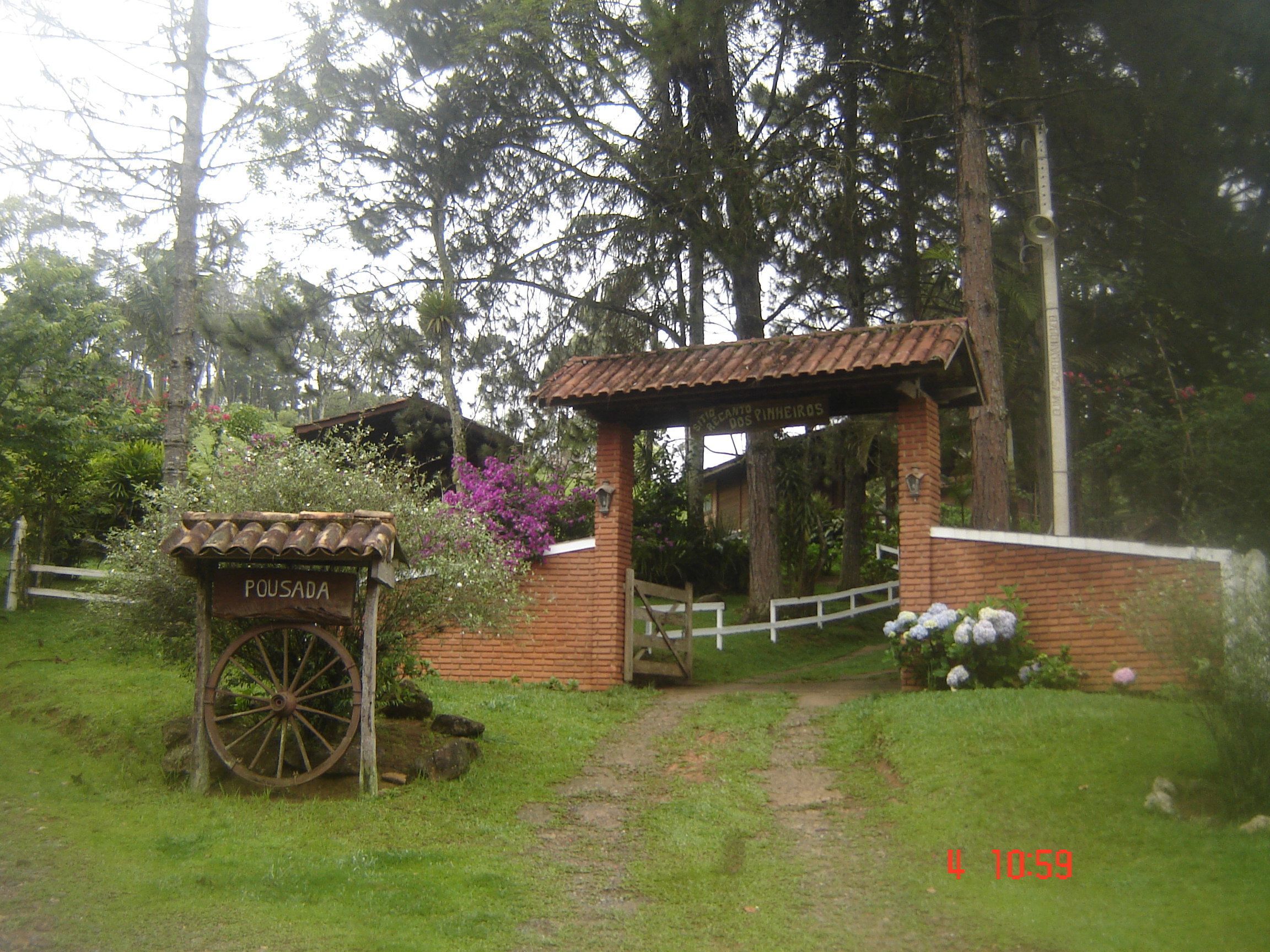 Une porte en bois rustique, sur laquelle on peut lire l’inscription « POUSADA », mène à un jardin luxuriant, avec un bâtiment en briques et une clôture en bois.