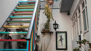 Una escalera exterior estrecha con barandillas de colores, plantas en macetas y un farol fijado a la pared.